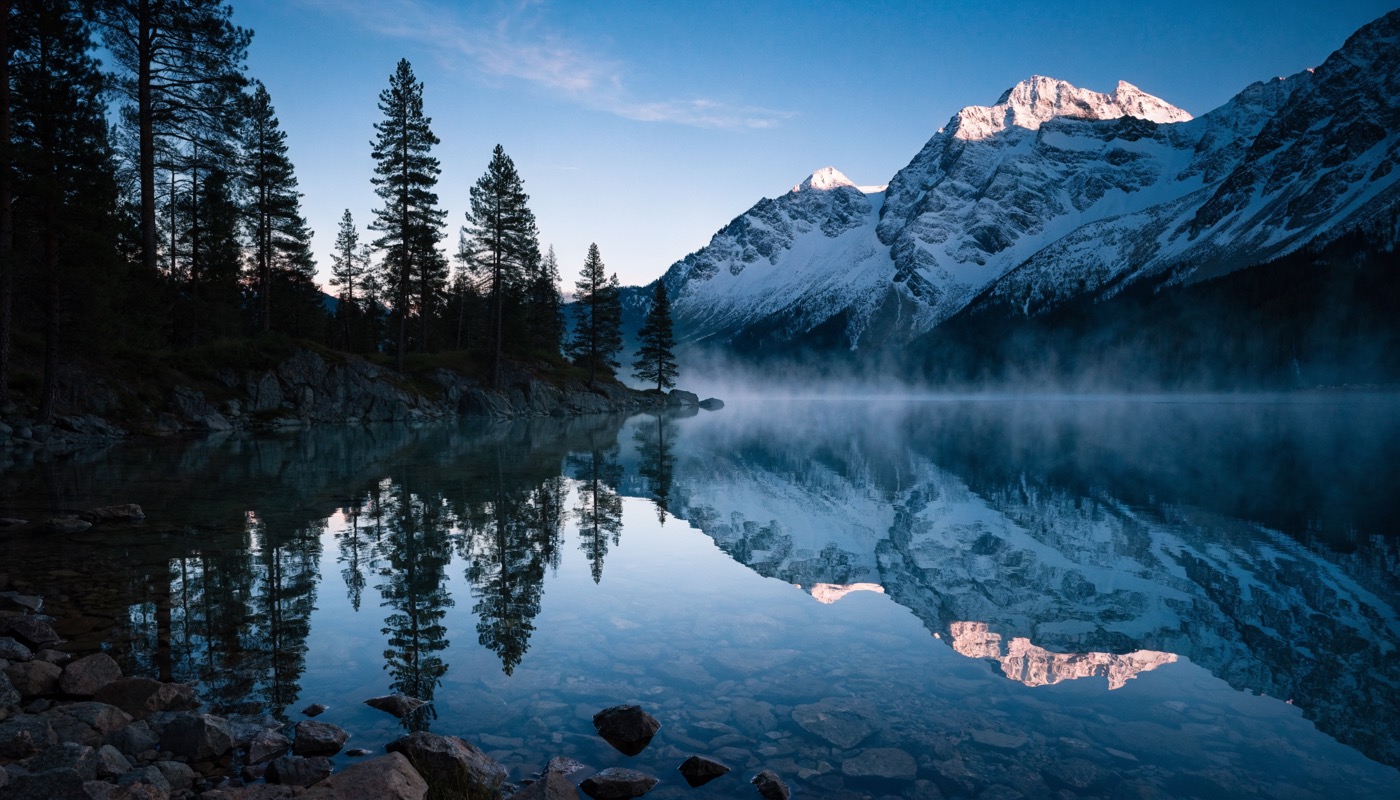 Photographic image of an alpine lake at dawn, first light on still water